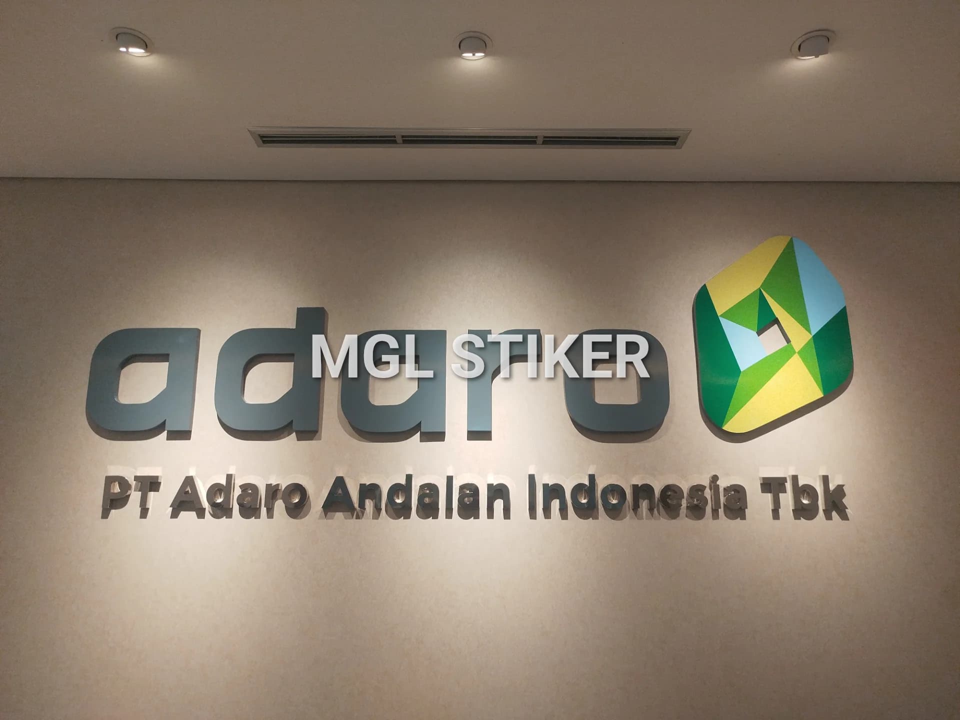 Huruf timbul 3D logo dan nama Adaro, beserta tulisan 'PT Adaro Andalan Indonesia Tbk' berwarna abu-abu gelap dan logo ikonik di dinding kantor, menunjukkan profesionalisme. Layanan pengerjaan huruf timbul berkualitas oleh MGL Stiker.